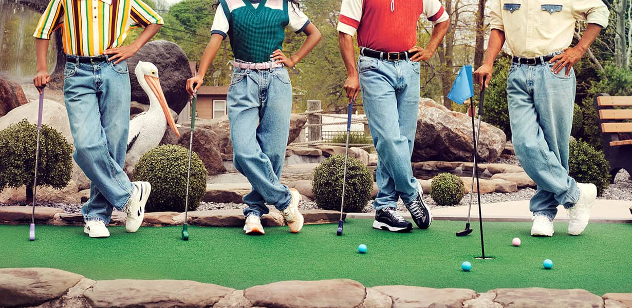 Four people wearing blue jeans and holding mini golf clubs on mini golf course