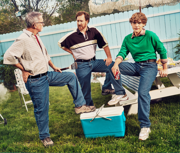 A grandfather, father, and son wearing blue jeans and standing by a cooler outside image